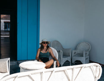 Woman sitting on chair against wall