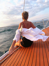 Rear view of woman sitting on pier over sea against sky