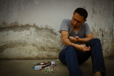 Man injecting syringe while sitting against wall