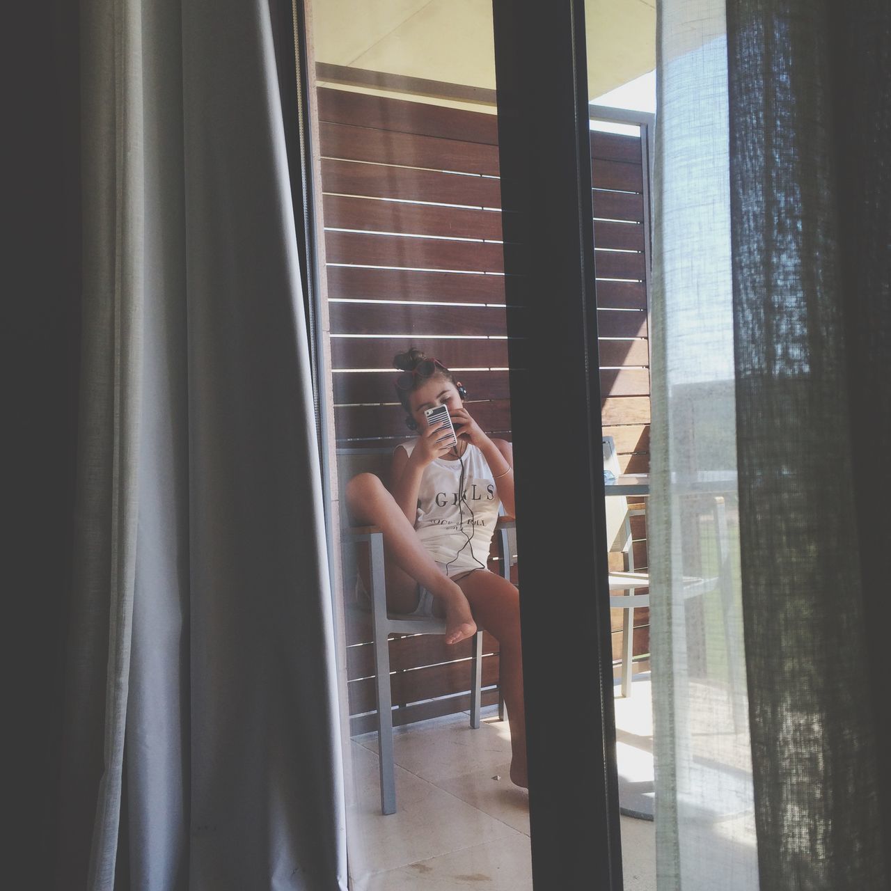 indoors, window, lifestyles, young adult, leisure activity, glass - material, young women, transparent, sitting, home interior, casual clothing, person, curtain, looking through window, reflection, architecture, standing