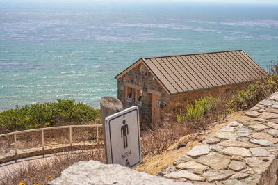 High angle view of sign against public restroom and sea on sunny day