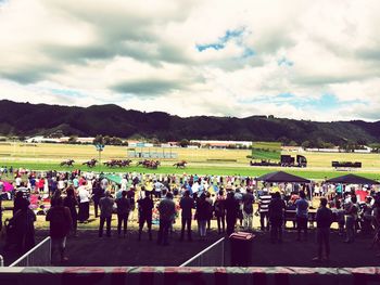 People on grassy field against cloudy sky