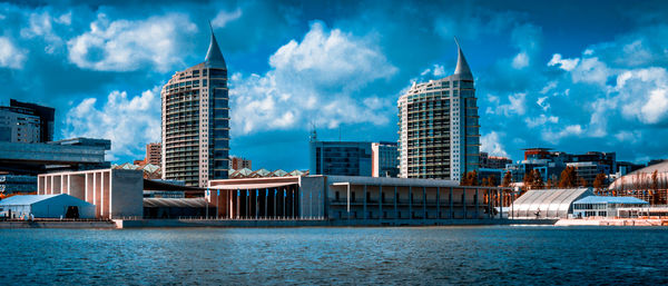 Modern buildings by river against sky in city