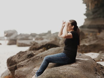 Man sitting on rock at beach against sky