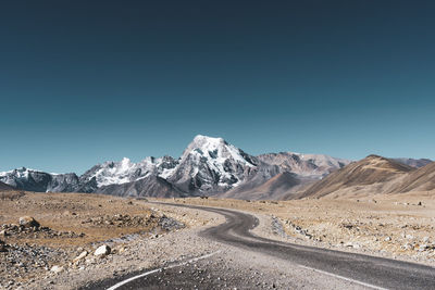 Road leading towards mountains against clear blue sky