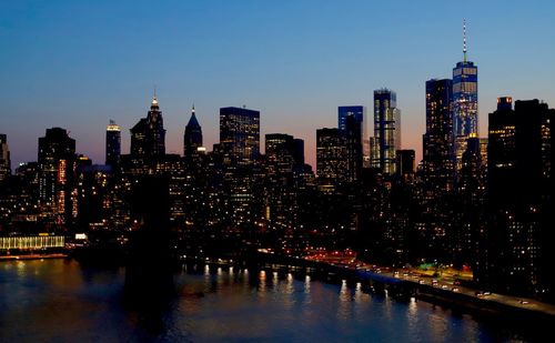 Illuminated buildings by river against sky in city