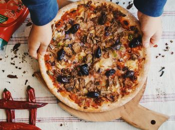 Cropped hands of man holding pizza on table