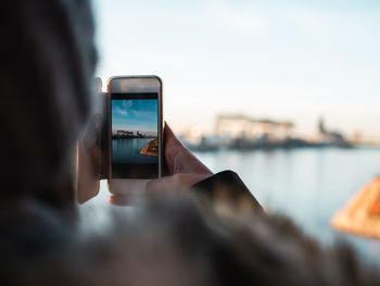 Close-up of woman photographing sea on mobile phone against sky