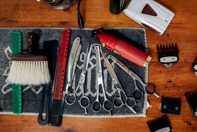 Top view of various barber instruments including scissors trimmers combs razor and brush placed on towel on wooden table in grooming salon