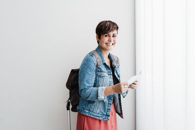 Woman holding smart phone while standing against wall