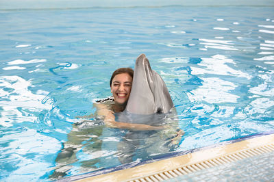 Smiling young woman with dolphin swimming in pool