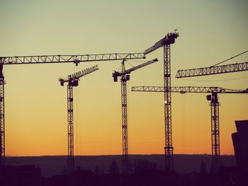 Cranes against sky at sunset