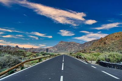 Empty road leading towards mountains against sky