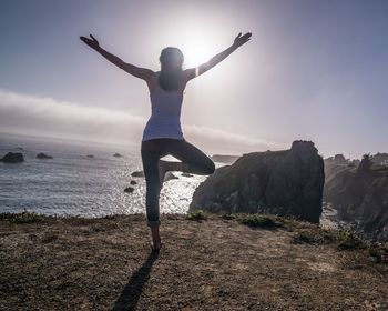 Rear view of man with arms raised at beach against sky