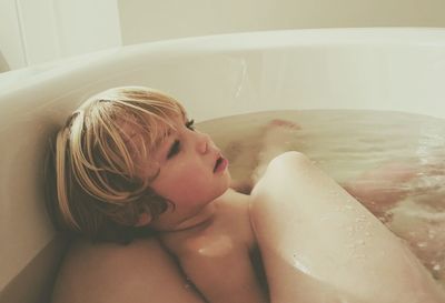 Low section of mother with son relaxing in bathtub at home