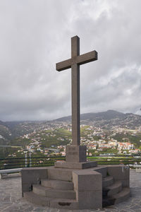 Cross in cemetery against building against sky