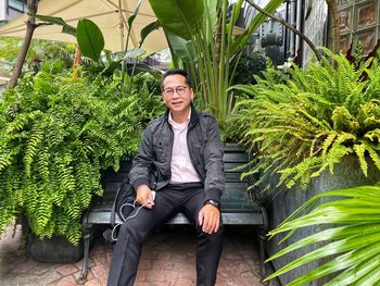 Portrait of mature man sitting on bench against plants