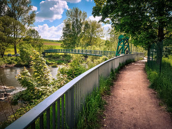 Footbridge over river amidst trees against sky