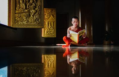 Monk reading book while sitting on floor in monastery