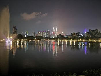 Illuminated buildings by river against sky at night