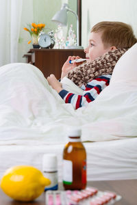 Side view of boy holding thermometer in mouth relaxing on bed at home