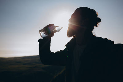 Reflection of woman drinking water on glass against sunset sky