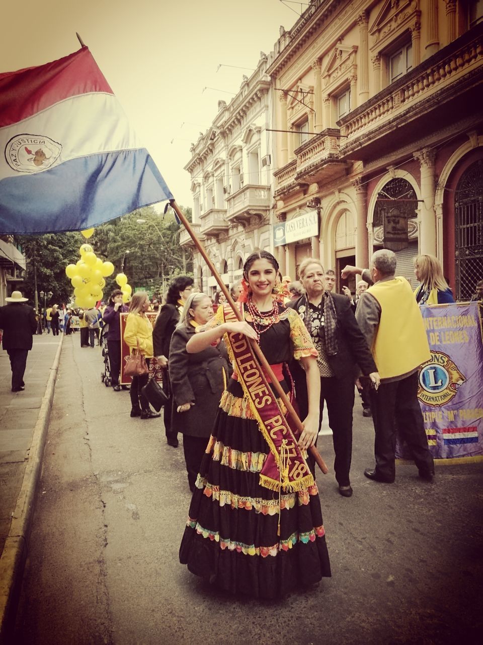 real people, men, women, built structure, lifestyles, architecture, traditional clothing, flag, building exterior, cultures, togetherness, leisure activity, walking, celebration, day, tradition, full length, outdoors, large group of people, yellow, sky, adult, adults only, people