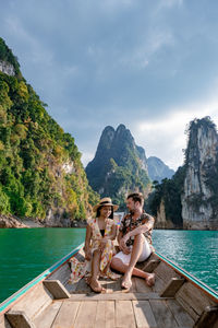 Couple sitting on mountain by sea against sky