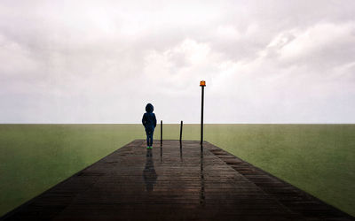 Rear view of woman walking on pier over sea against sky