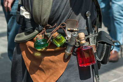 Midsection of man with perfume bottles and dagger standing outdoors