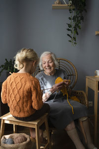 Happy grandmother teaching granddaughter to knit at home