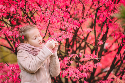 Low angle view of woman holding pink flower by tree
