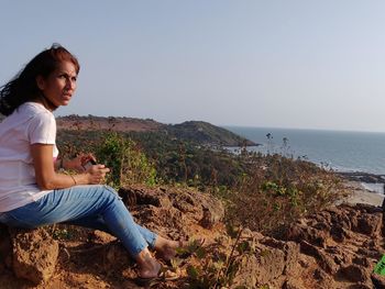 Woman sitting on rock by sea against clear sky