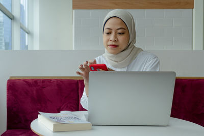 Young woman using phone while sitting on table