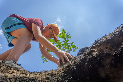 Low section of woman sitting on rock against sky