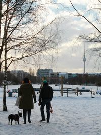 People with dog standing on field in city against sky during winter