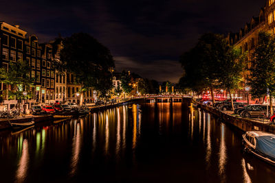 Boats moored in canal amidst illuminated buildings in city at night