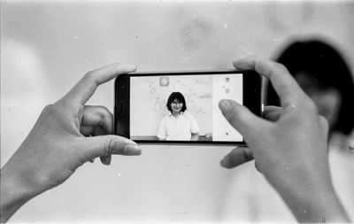 Cropped hands of woman photographing friend with mobile phone