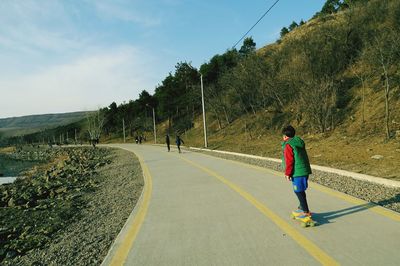 Rear view of man skateboarding on road against sky