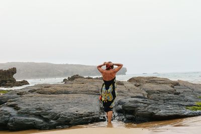 Rear view of shirtless man standing on beach against clear sky