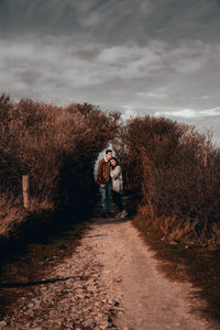 Man standing on footpath amidst plants against sky