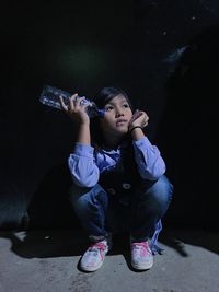 Thoughtful girl with bottle crouching against wall