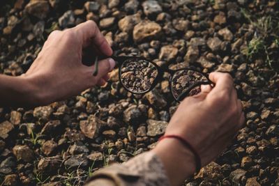 Cropped hands of person holding eyeglasses over rocks