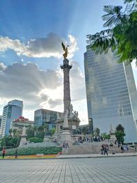 Statue of buildings in city against cloudy sky