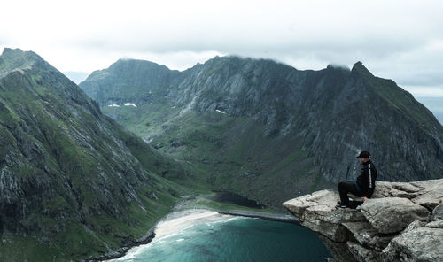 Rear view of man sitting on mountain against sky