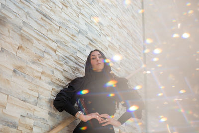 Portrait of young woman standing against wall