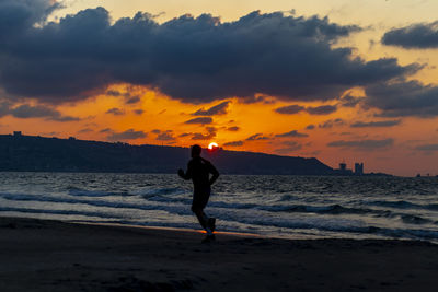 Full length of woman standing on beach against sky during sunset