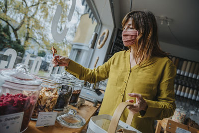 Mature female customer in mask picking up food while shopping in zero waste store during pandemic