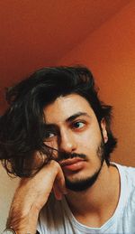 Low angle view of young man with hand on chin against wall at home