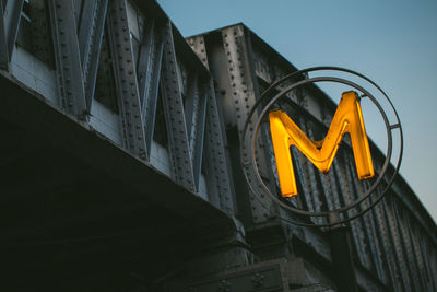 Low angle view of illuminated letter m on bridge against sky